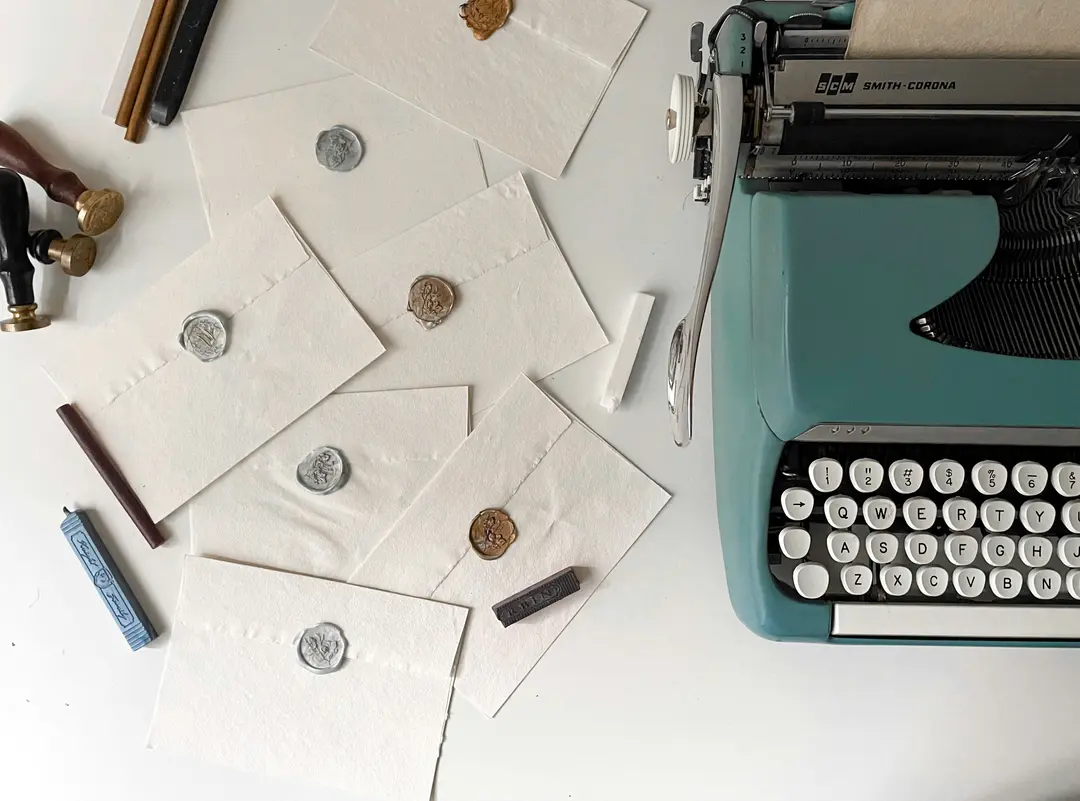 fotografia de uma máquina de escrever, cercada de envelopes selados com lacres de cera